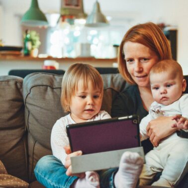 Mom sitting on sofa with two kids on her lap looking at a tablet