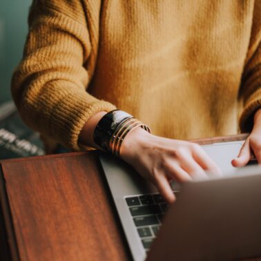 Person with bracelets and yellow sweater typing on laptop