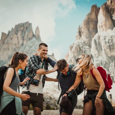 Four people standing and laughing in front of a mountain