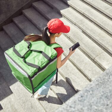 Overhead view of delivery person carrying pack on back and looking at phone