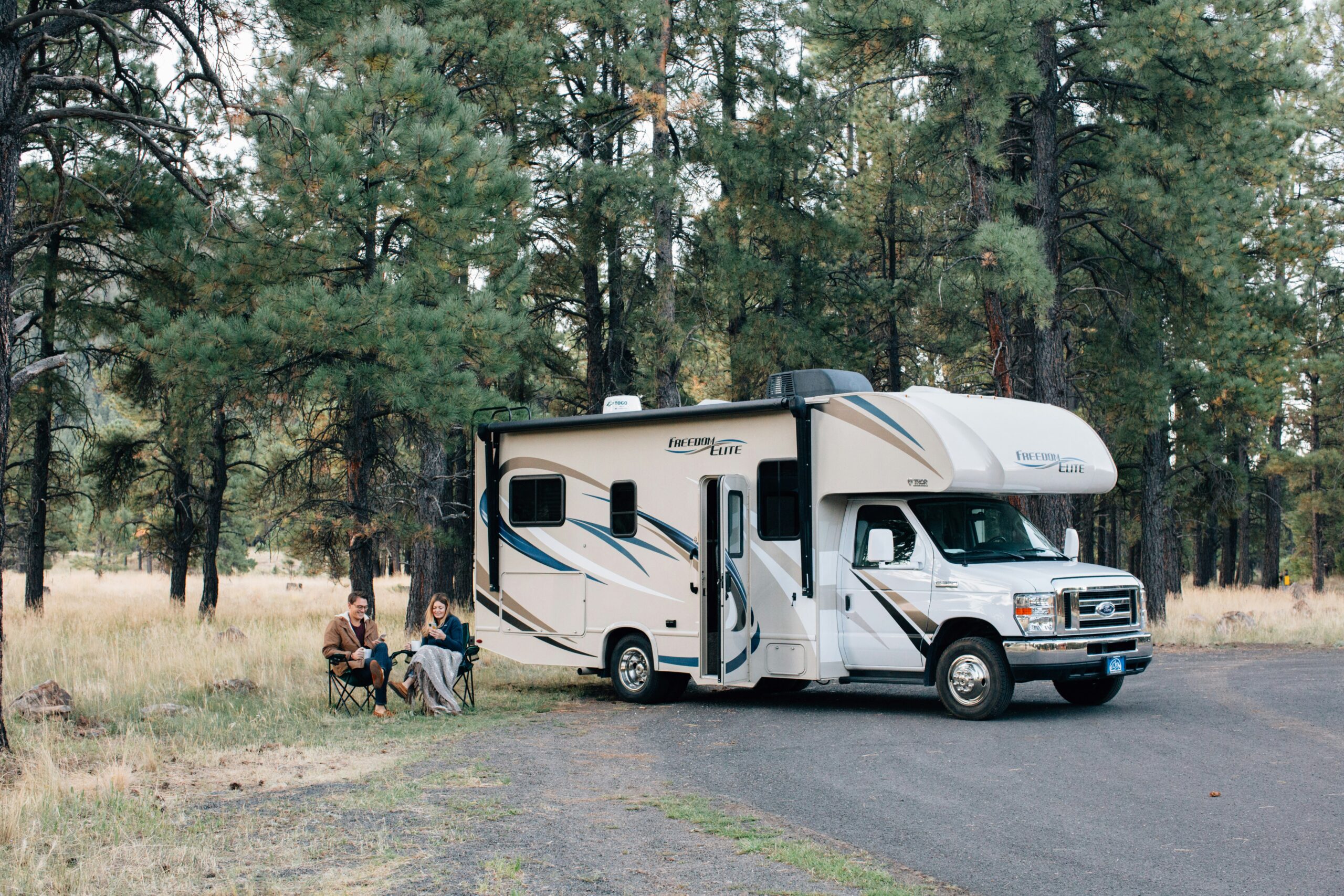 people sitting next to a white rv in the woods
