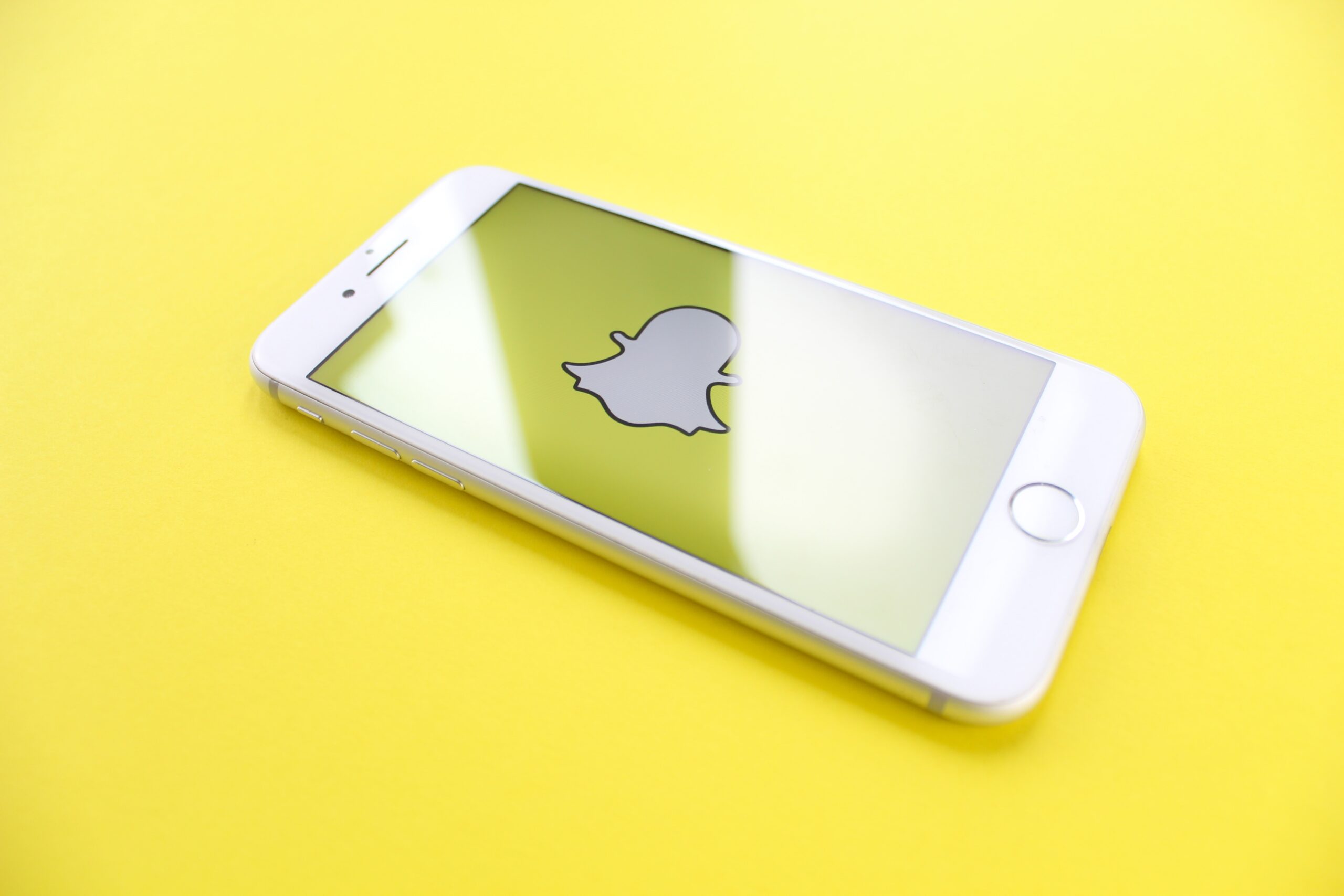 White iphone sitting on yellow background with Snapchat open